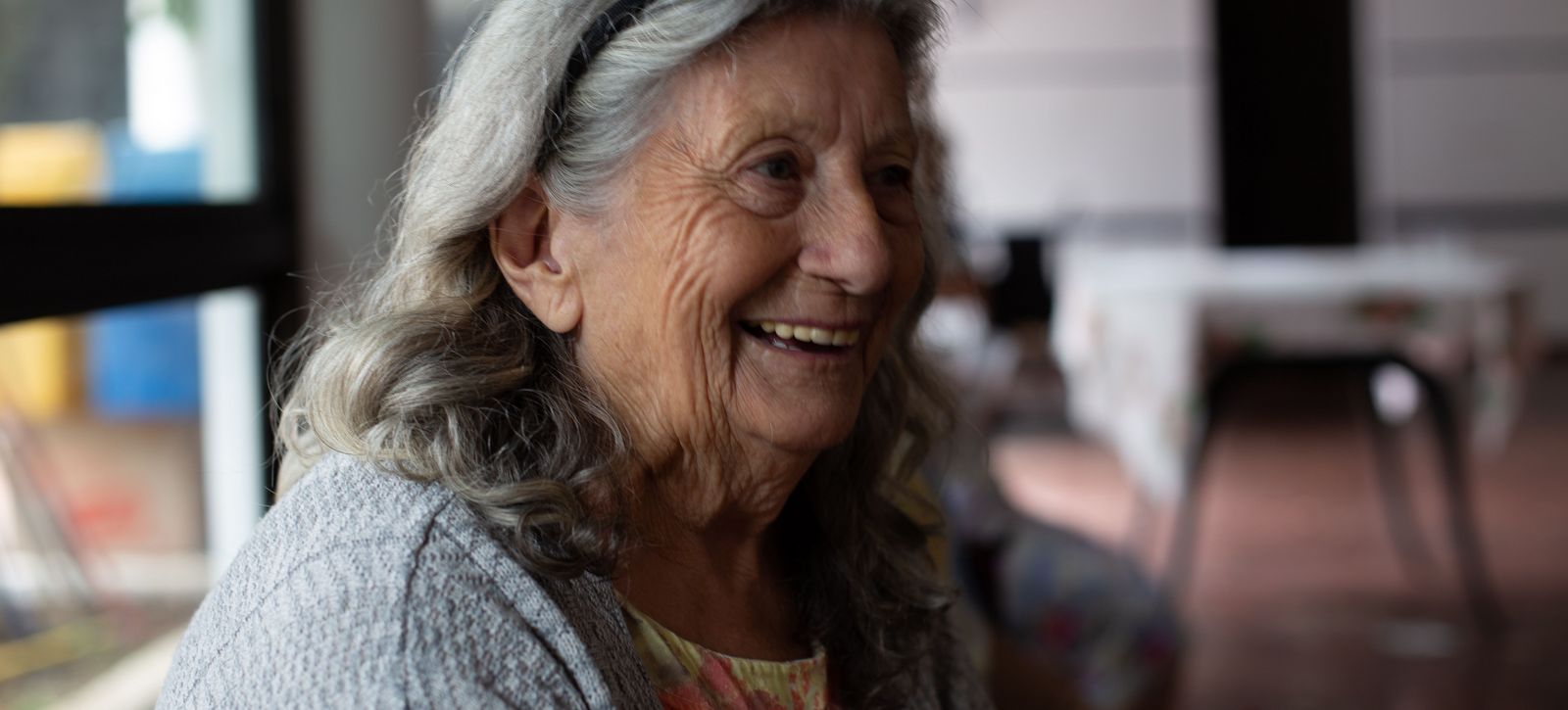 Eine ältere Frau mit grauen Haaren lächelt zufrieden.